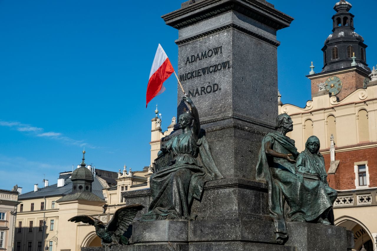 Monument of Adam Mickiewicz in Kraków, featuring Polish flag and historic architecture.